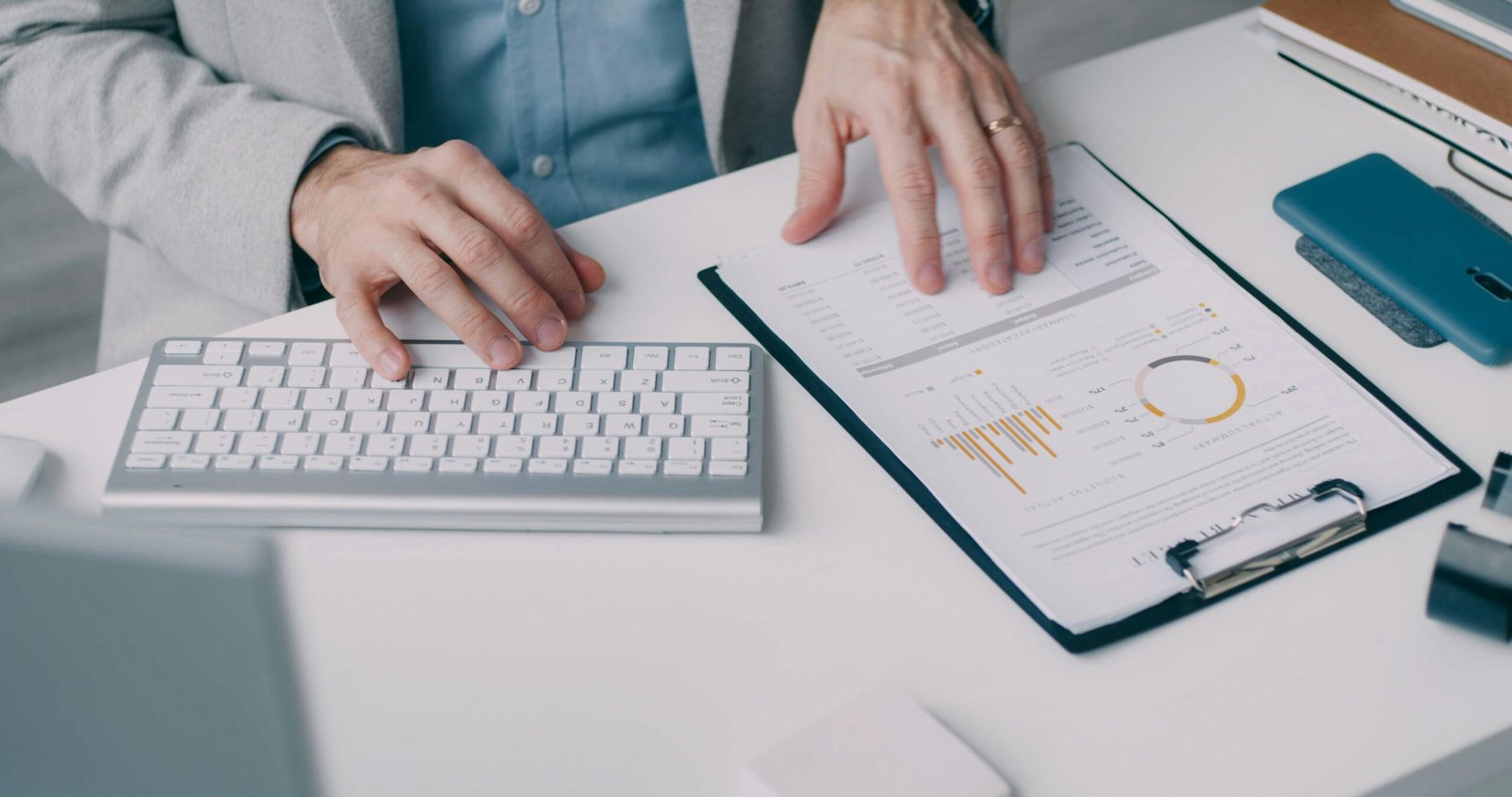 Picture of man's hands with one on a keyboard and the other examining page with charts